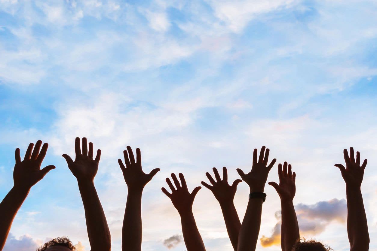 Many hands raised against a bright sky